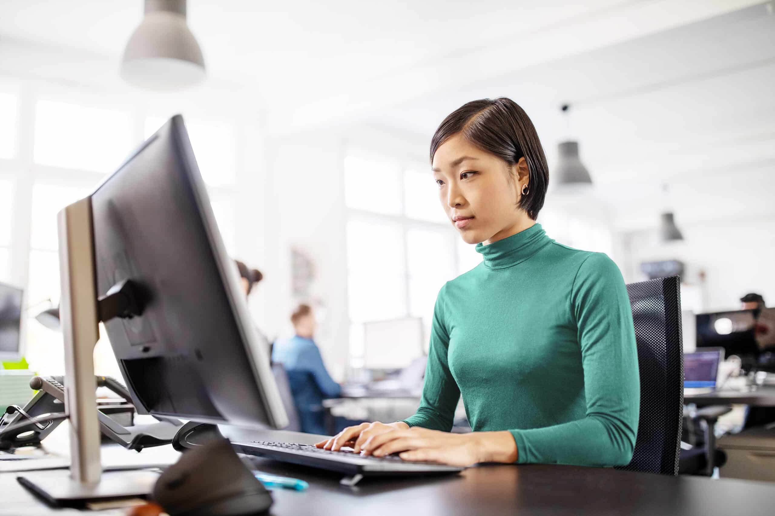 Person in office setting looking at computer screen and typing