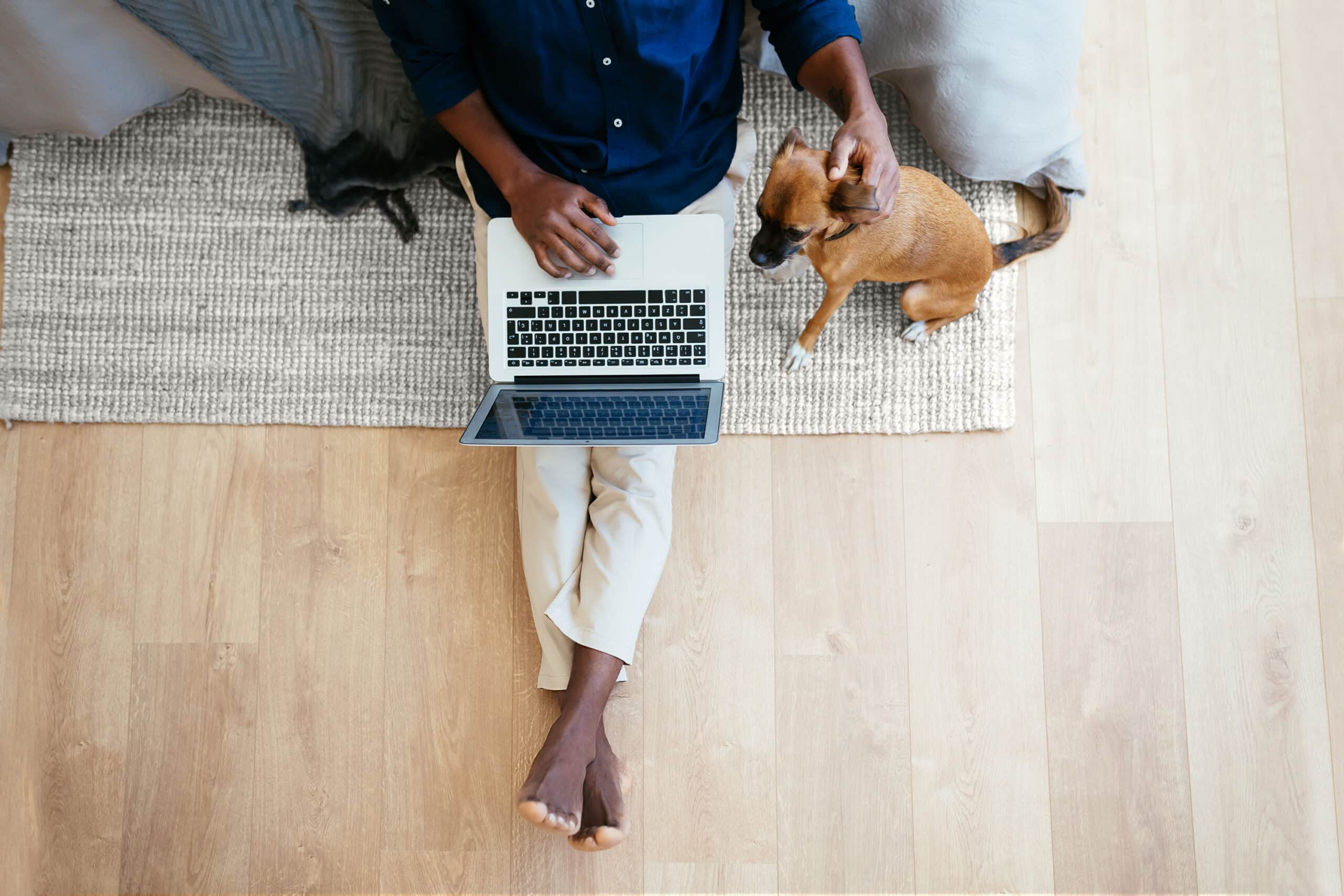 Person sitting on the floor in front of laptop, petting a dog