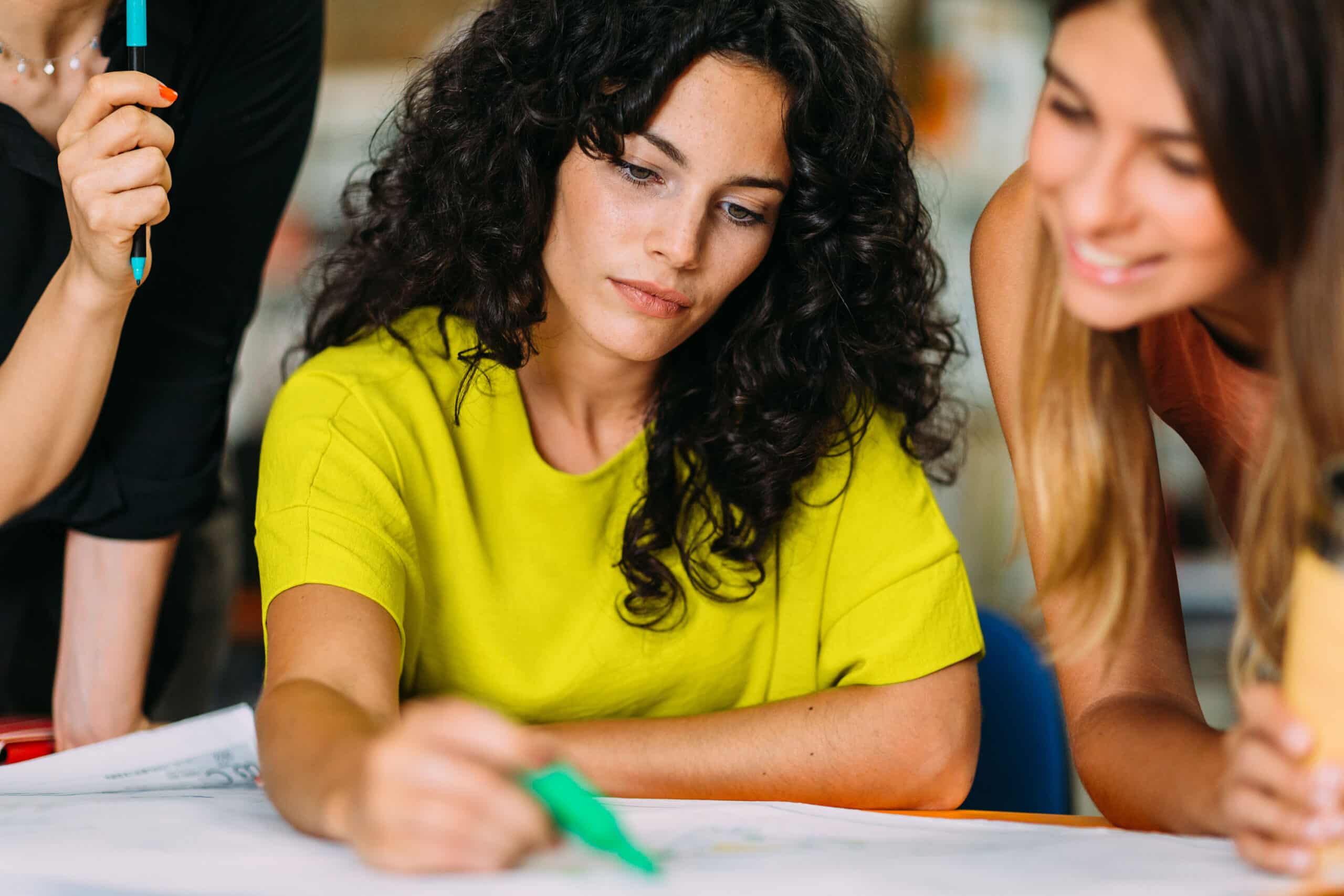 person holding marker in front of paper next to other people