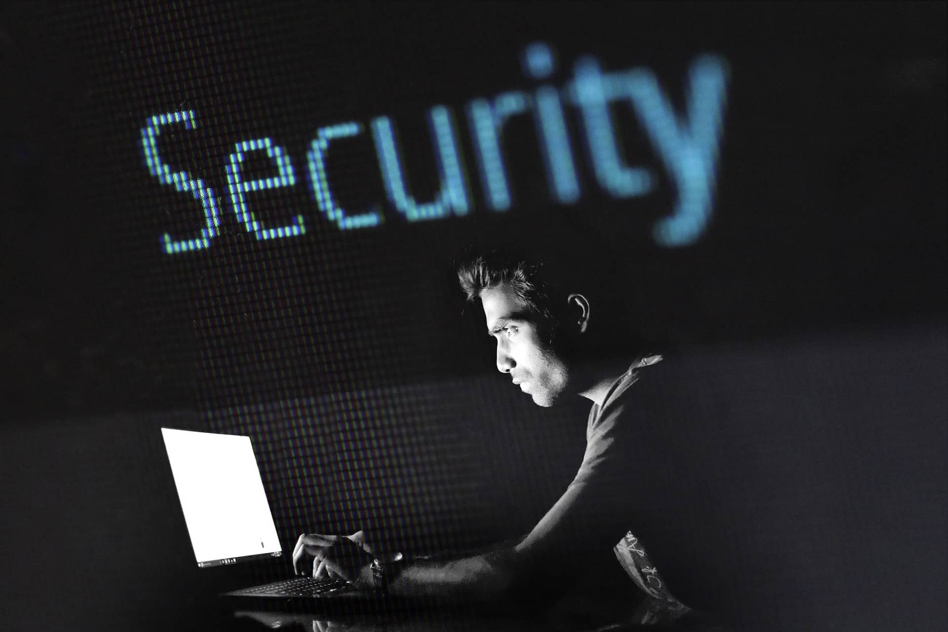 Person in front of laptop in a dark room, the word security in the background