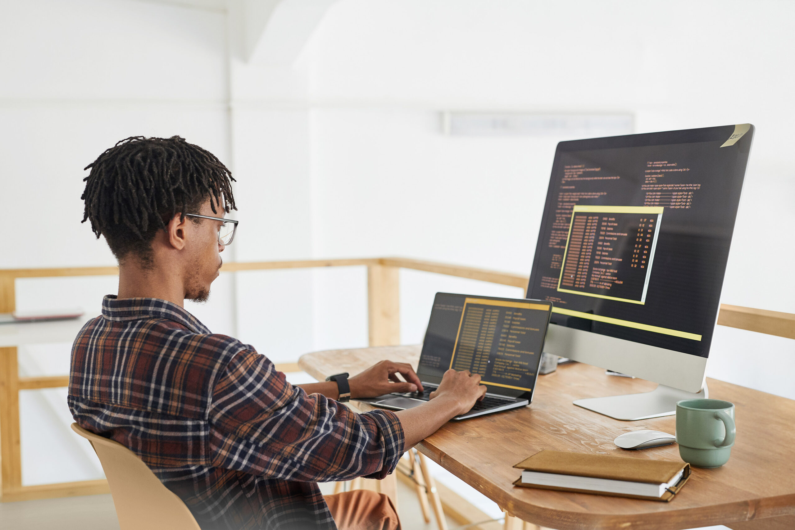 Person in front of desktop and laptop coding