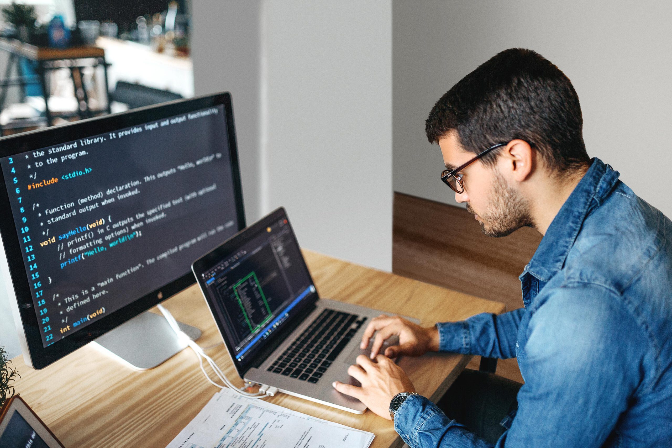 Person in front of laptop and desktop displaying code 