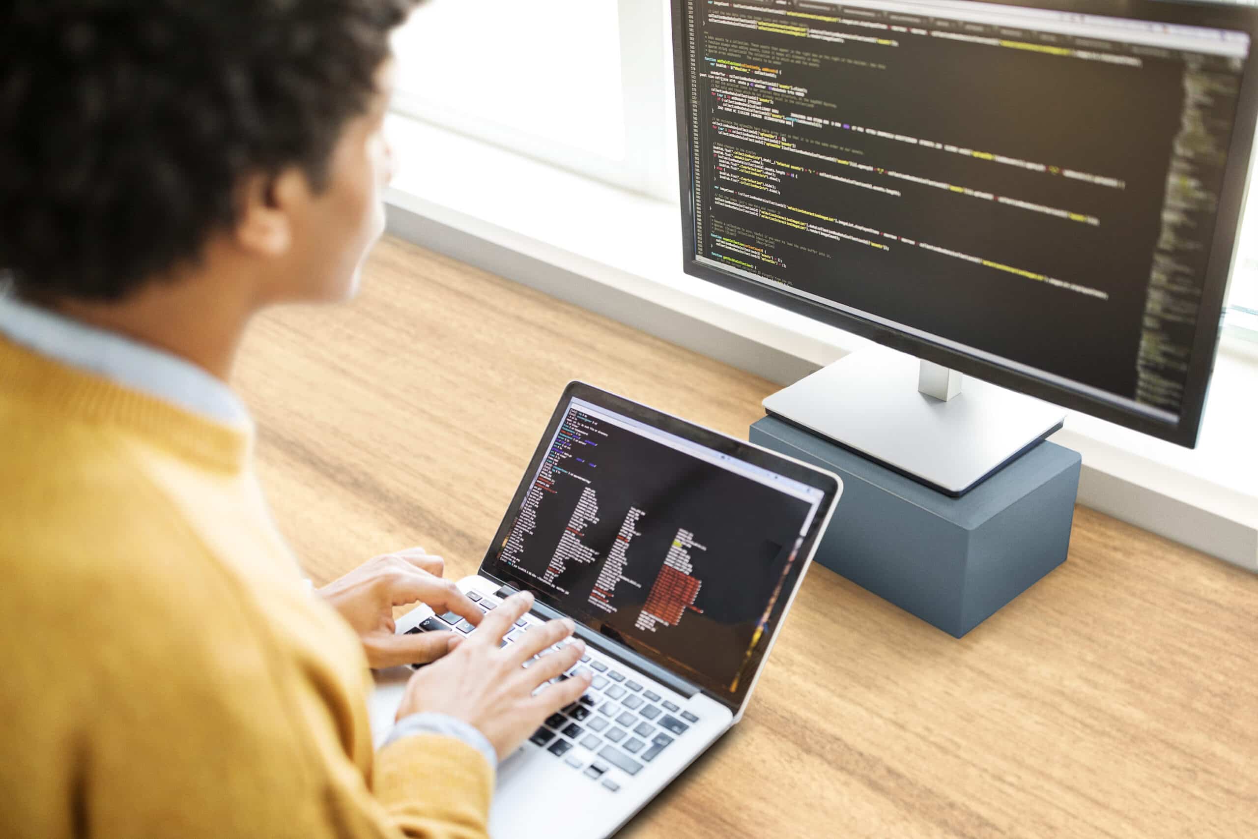 Person in front of laptop and desktop with code displayed on them